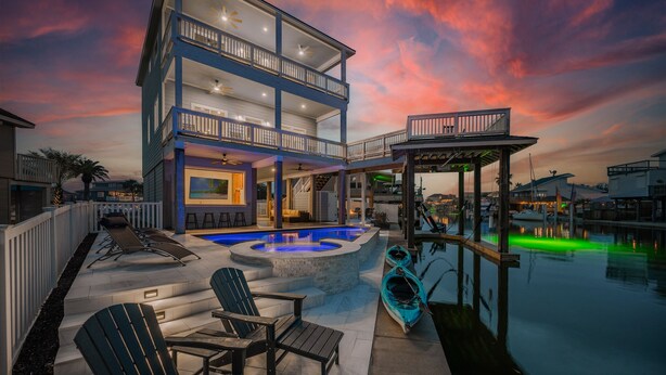 Ein zweigeschossiges Haus mit Pool, Sitzgelegenheit im Freien und einem überdachten Bereich am Wasser.