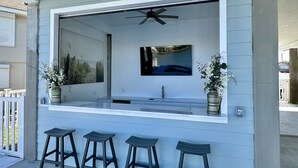 Ein moderner Außenbereich mit Bar, ausgestattet mit einem großen Fenster, Deckenventilator und drei Barhocker.