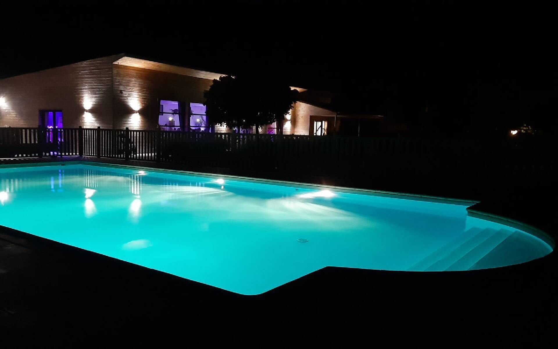 Una piscina de borde curvo, rodeada por una valla y un edificio con ventanas iluminadas.
