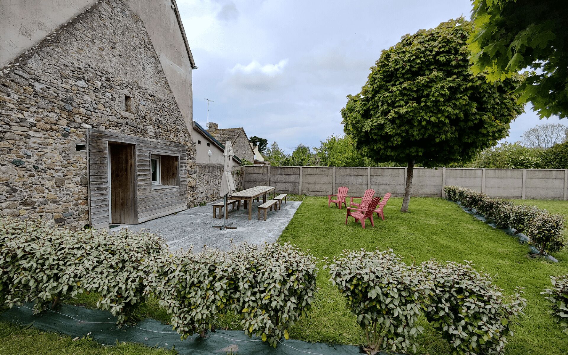 A stone building with a wooden door, a patio with a table and chairs, and a well-maintained lawn with hedges.