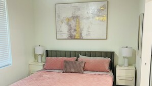 A bedroom with a bed, a ceiling fan, a wall-mounted abstract painting, and bedside lamps.