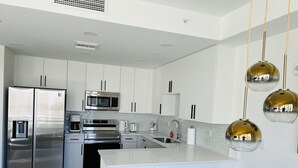 A modern kitchen with stainless steel appliances, white cabinetry, and a central island with a sink.