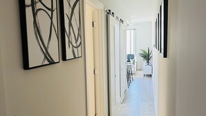 A hallway with wooden flooring, white walls, and black abstract paintings.