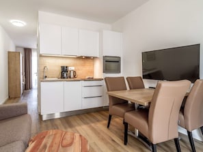 Eine moderne Küche mit weißen Schränken, einer Holz Arbeitsplatte und einem eingebauten Backofen. Es gibt einen Esstisch mit vier Stühlen und einen flachbildfernseher an der Wand.