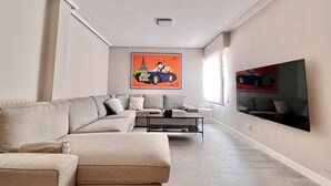 Een moderne woonkamer met een beige hoekbank, een salontafel en een flatscreen televisie aan de muur.
