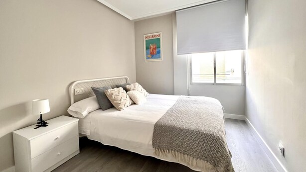 Een slaapkamer met een bed, nachtkastje, lamp en een raam met een blind.