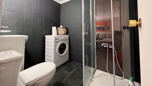 Een badkamer met toilet, wasmachine en douchecabine.