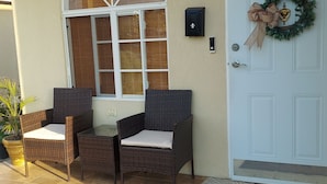 A front porch with wicker furniture, a large arched window, a white door with a wreath, and a doormat. - SUPREME LIVING VACATION HOME. Your home away from home!  (Portmore)