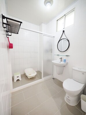 Un baño con ducha, inodoro, lavamanos y un pequeño taburete.