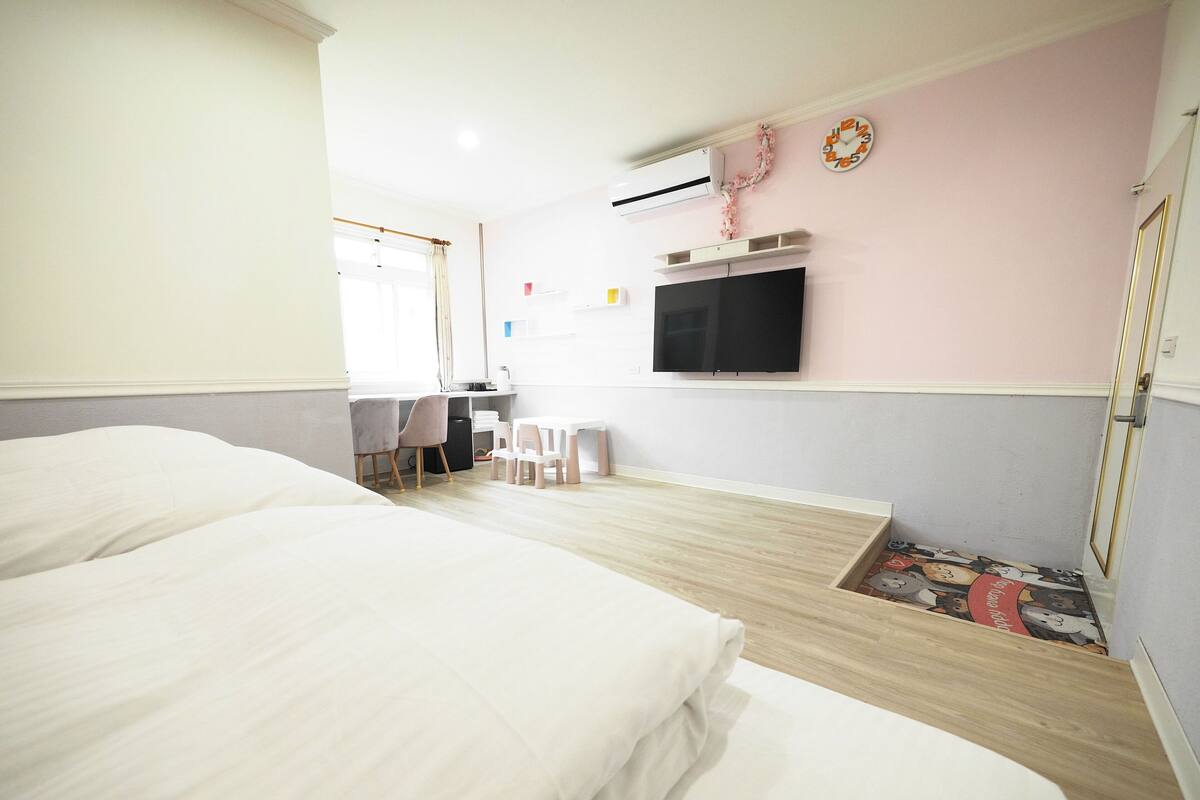 A hotel room with two beds, a desk, a chair, a TV, and a small table.