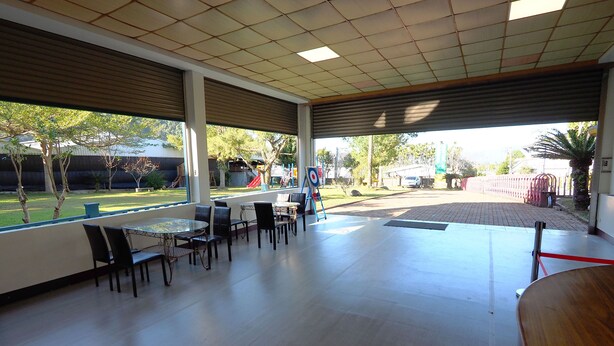 A covered outdoor seating area with tables and chairs, large windows, and a view of a playground. - Sun Moon Cat (Yuchi)