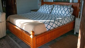 A wooden bed with a patterned bedspread and pillows, a nightstand, a chair, and a rug.