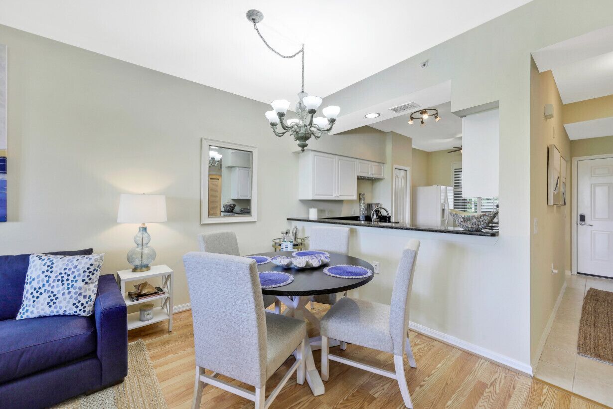 A modern living room with a dining area, a chandelier, and a kitchen in the background.