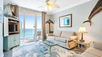 Relax in a comfortable seating area with a sofa, armchair, and glass coffee table, offering a serene view of the ocean from the adjacent balcony.