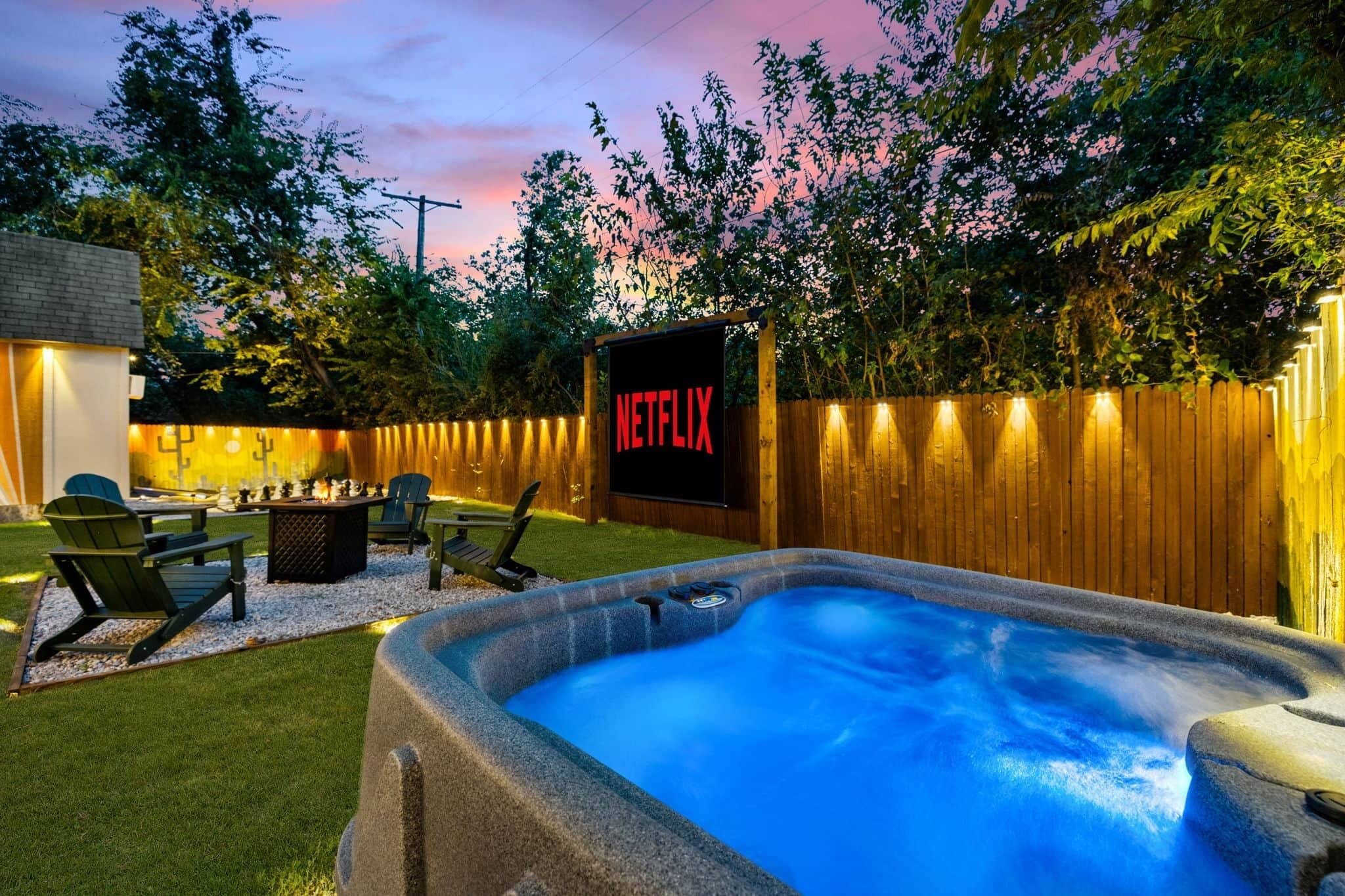 A backyard with a hot tub, outdoor seating, a wooden fence, and a Netflix sign.