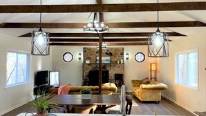 A spacious living room with a stone fireplace, wooden beams, and modern lighting fixtures. - Modern, family-friendly, nature packed getaway (Berkeley Springs)