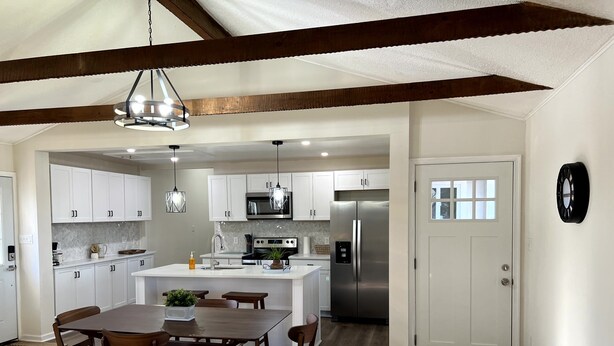 A modern kitchen with white cabinets, a stainless steel refrigerator, and a dining area with wooden chairs and a table. - Modern, family-friendly, nature packed getaway (Berkeley Springs)