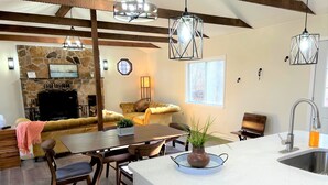 A modern kitchen with a central island, a stone fireplace, and a dining area with a sofa and chairs. - Modern, family-friendly, nature packed getaway (Berkeley Springs)