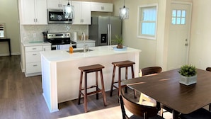A modern kitchen with white cabinetry, stainless steel appliances, and a central island with stools. - Modern, family-friendly, nature packed getaway (Berkeley Springs)