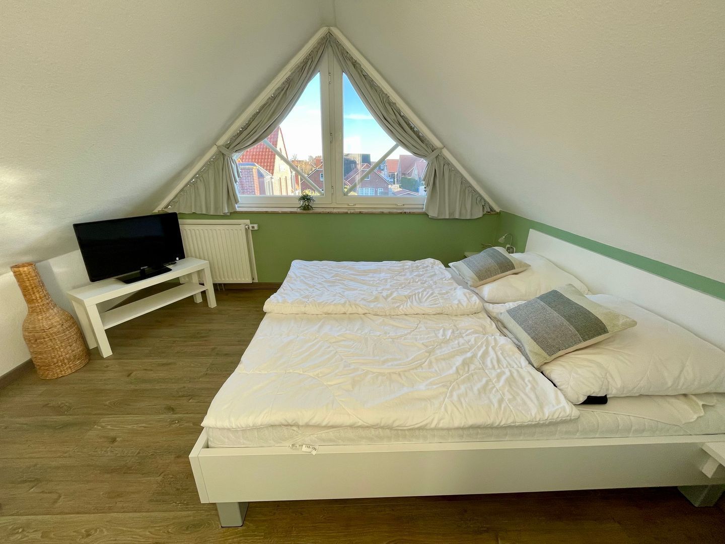 A bedroom with a bed, a TV, a small table, and a window with curtains.