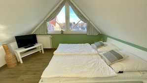 Un dormitorio con cama, televisor, una mesita y una ventana con cortinas.