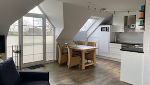 Una cocina moderna con armarios blancos, encimera negra y microondas. Hay una zona de comedor con una mesa y sillas de madera.