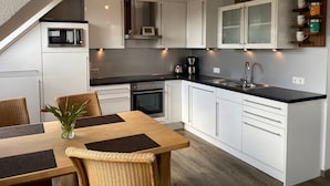 Una cocina moderna con armarios blancos, encimera negra y un comedor con sillas de mimbre y una mesa de madera.