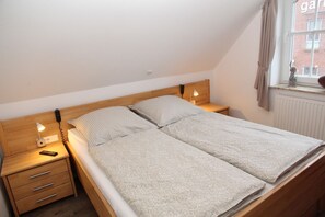 Una cama de matrimonio con dosel de madera, dos mesitas de noche con lámparas y una ventana con vista a un edificio de ladrillo.