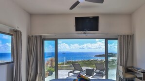 Ett hotellrum med en säng, en takfläkt, en TV och en balkong med utsikt över havet.