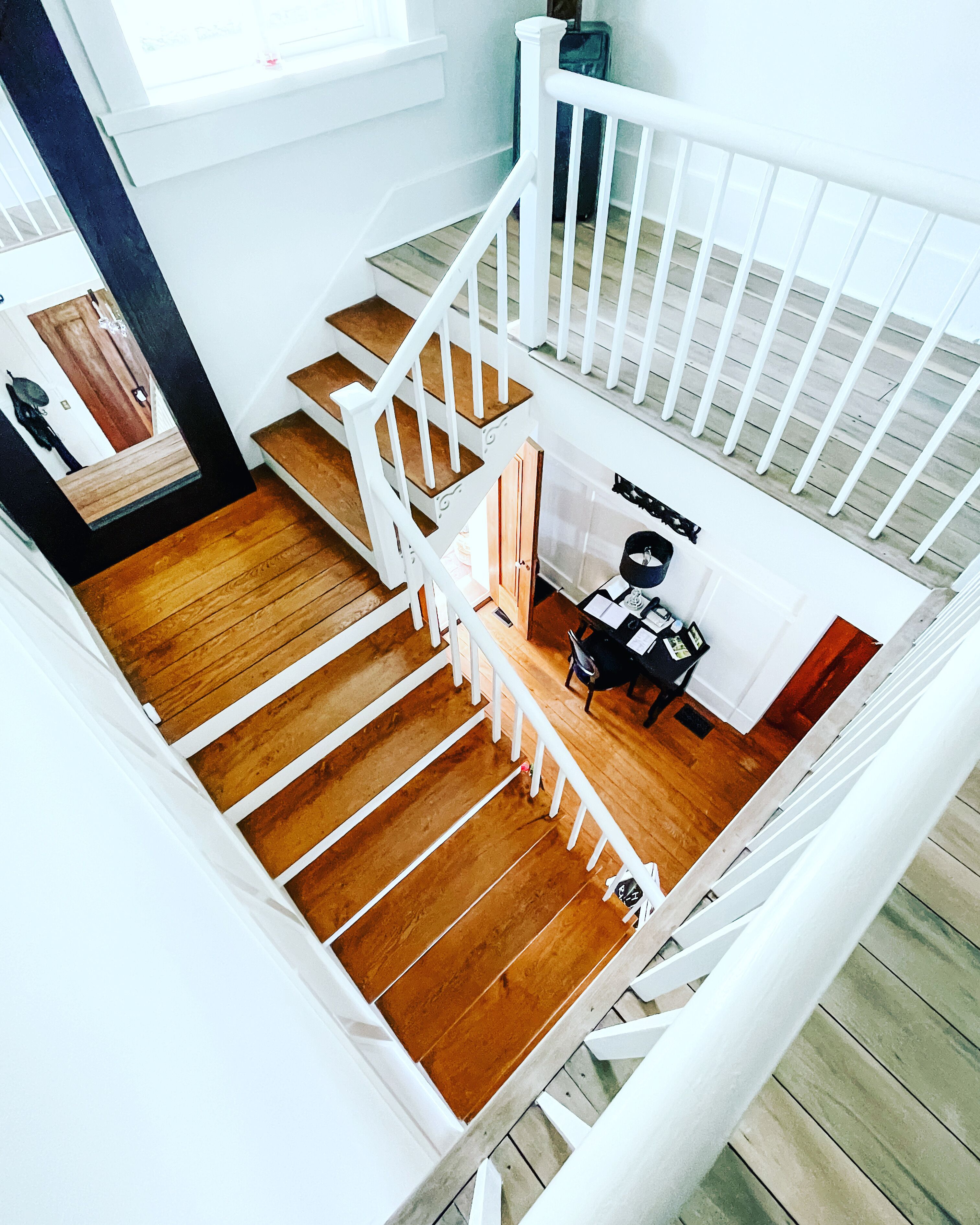 Un escalier en bois à plusieurs niveaux avec des rampes blanches, un bureau avec une chaise et une fenêtre en arrière-plan.