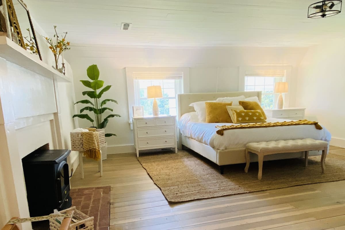 A bedroom with a bed, bedside tables, a fireplace, and a large window.