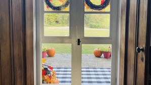 A wooden door with two glass panels, a wreath on each panel, and a small step leading to a porch with pumpkins and a checkered mat. - The Hopestead Bed & Breakfast (Fayetteville)