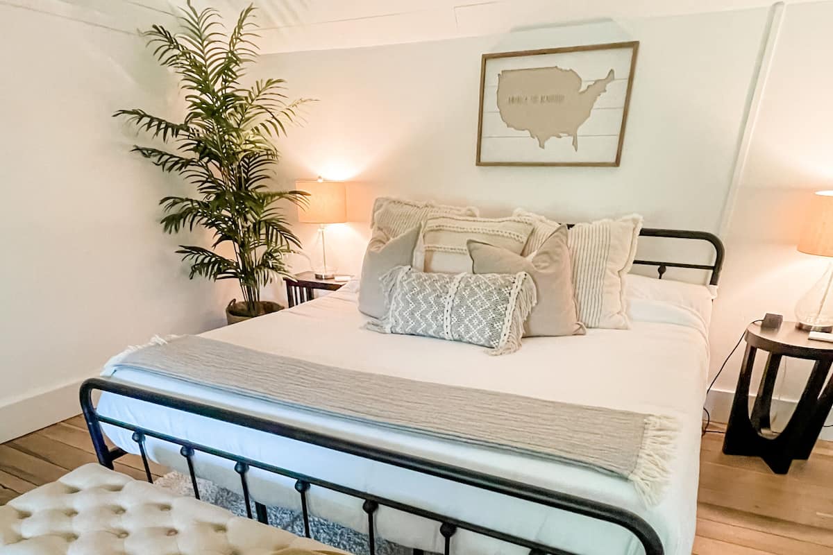 A bedroom with a bed, a bench with a hat, a potted plant, and a wall map.