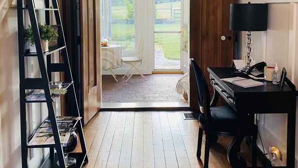 A room with a wooden floor, a desk with a lamp, a chair, and a bookshelf. There is a door leading to a balcony with a view of the outdoors. - The Hopestead Bed & Breakfast (Fayetteville)