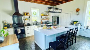 A spacious kitchen with a large island, wooden ceiling beams, and a stone floor. - The Hopestead Bed & Breakfast (Fayetteville)
