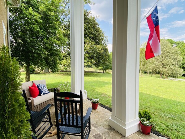 A covered porch with a bench, a chair, and a flag.