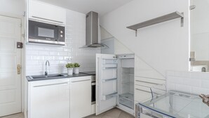 Et moderne køkken med hvide skabe, en Bosch mikrobølgeovn, en emhætte i rustfrit stål og et spisebord med glasplade.