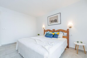 Een slaapkamer met een groot bed, een houten hoofdbord, twee bedlampen, een klein rond tafeltje met een plant, en een ingelijst kunstwerk aan de muur.