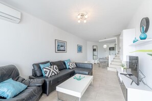 Een moderne woonkamer met een zwarte leren bank, een witte salontafel en een keuken met een wit aanrecht en een blauwe vaas.