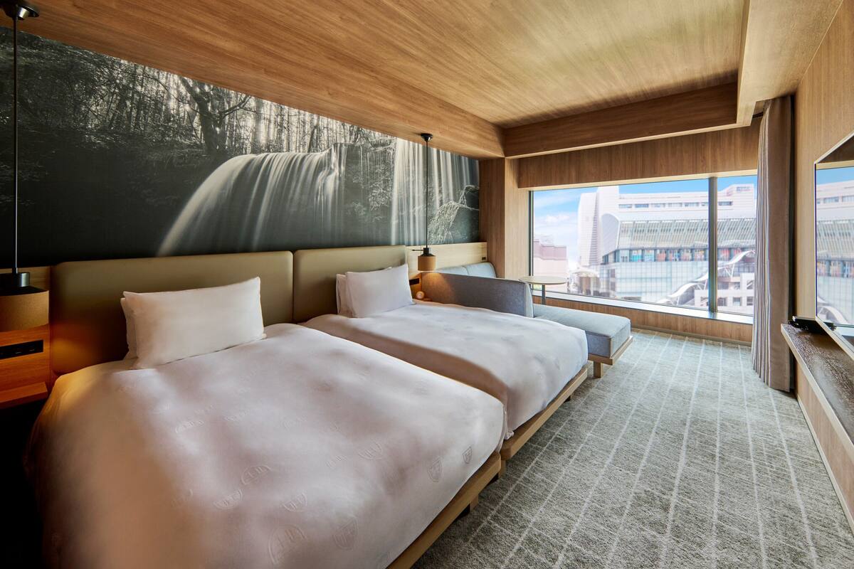 A hotel room with two beds, a large window with a city view, and a wall-mounted artwork.