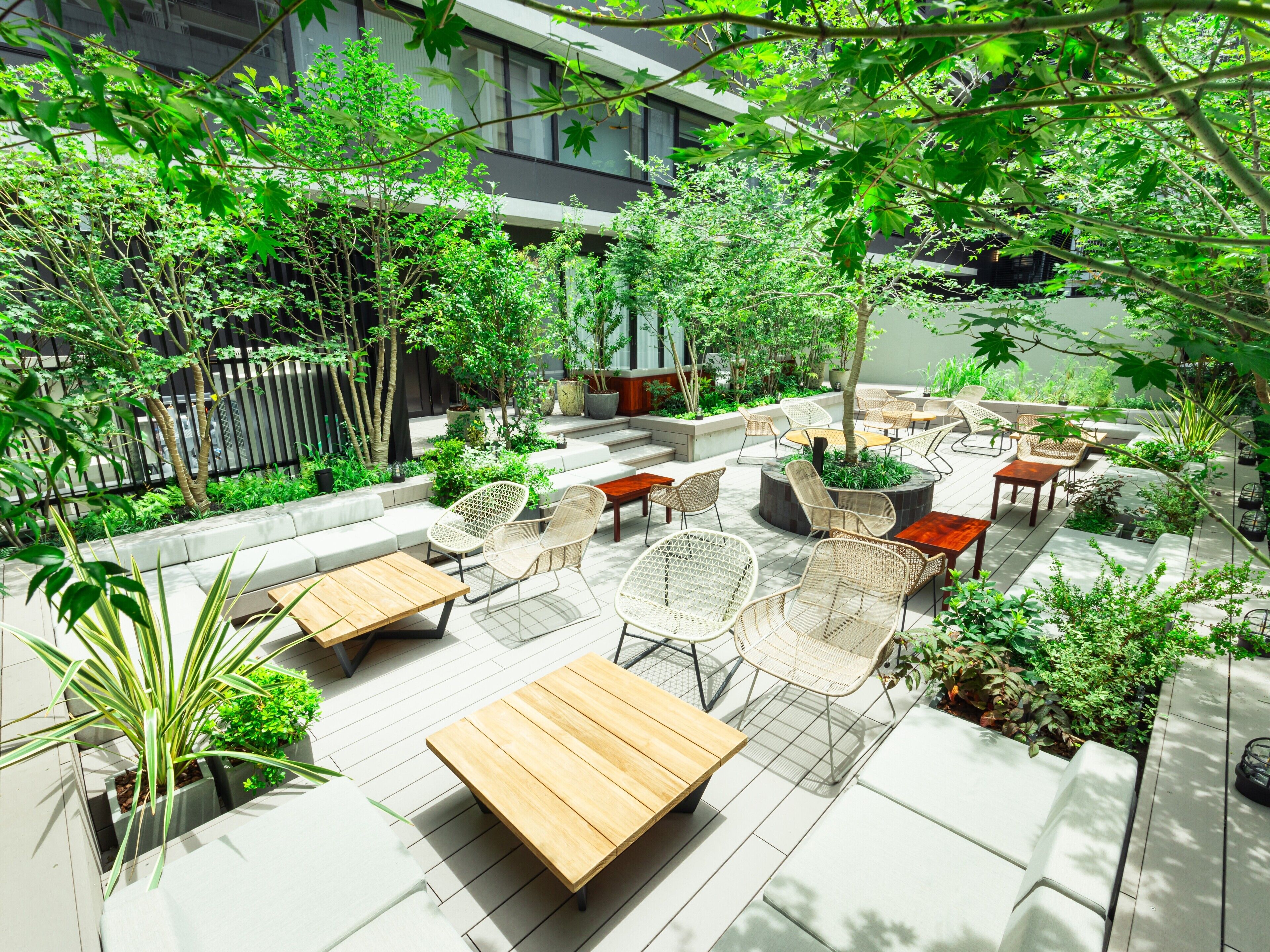 Un patio al aire libre con varias zonas de estar, incluyendo mesas y sillas, rodeado de abundante vegetación y plantas en macetas.