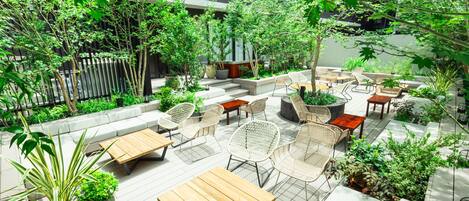 Un patio al aire libre con varias zonas de estar, incluyendo mesas y sillas, rodeado de abundante vegetación y plantas en macetas.