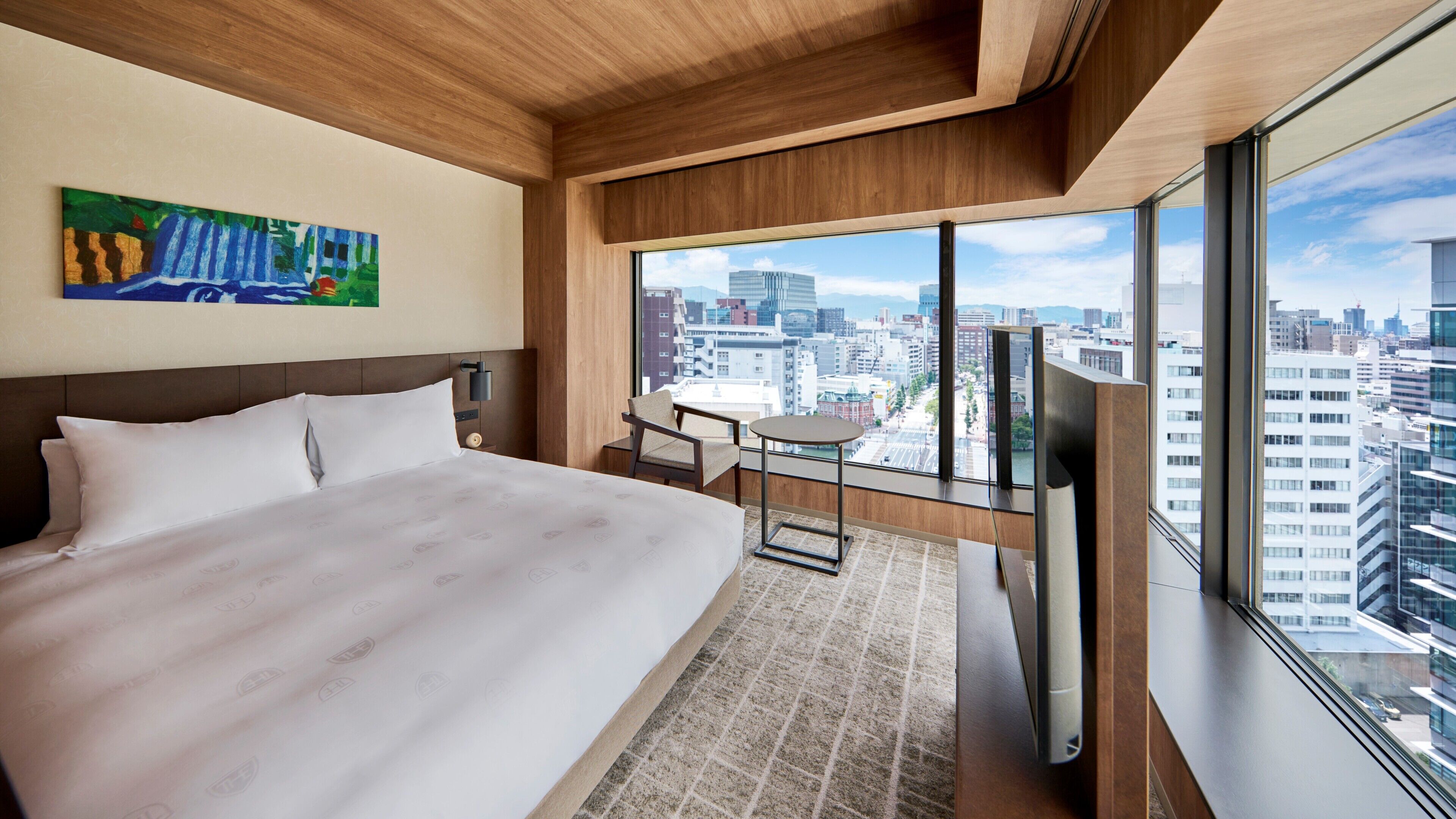 Une chambre d’hôtel avec un grand lit, une petite table, une chaise, une télévision et une vue sur la ville.