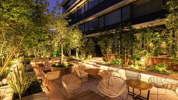 Relax in a serene outdoor space surrounded by lush greenery and comfortable wicker seating.