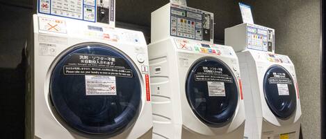 A row of identical white laundry machines with control panels and instructional labels.