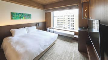A hotel room with a large bed, a flat-screen TV, a window with a view of buildings, and a painting on the wall.