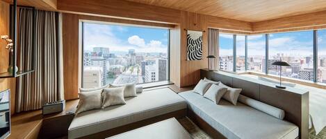 A modern hotel room with a large bed, a sofa, a small table, and a view of the city.