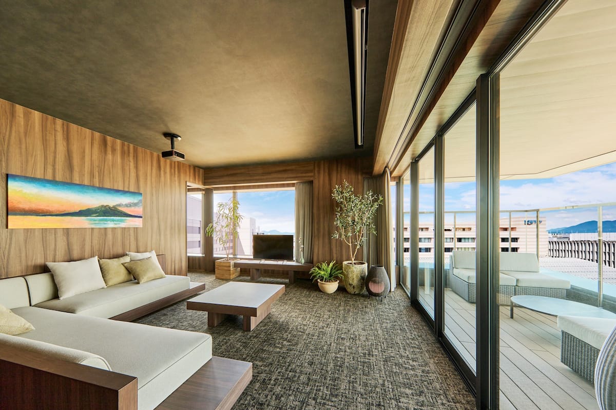 A modern hotel room with a large window, a sofa, a coffee table, and a TV.