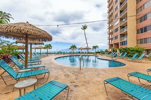A pool area with lounge chairs and thatched umbrellas, surrounded by a building with balconies. - 8th floor resort studio, AC, stunning ocean views, walkable area (Lahaina)