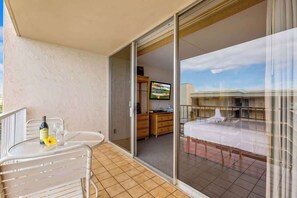 A balcony with a table and chairs, a bottle of wine, and a television in the background. - 8th floor resort studio, AC, stunning ocean views, walkable area (Lahaina)